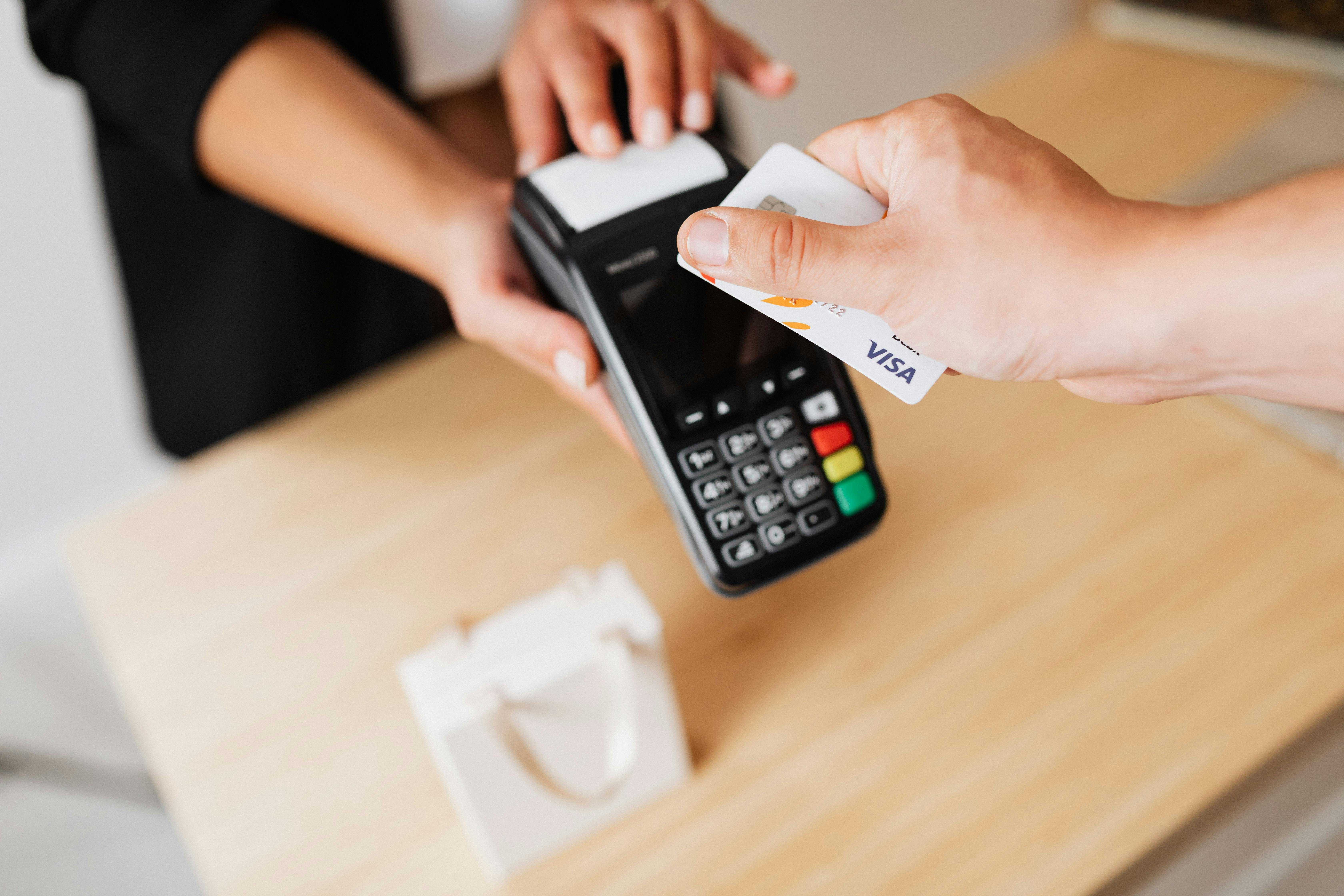 A customer tapping a Visa card on a payment terminal held by a cashier